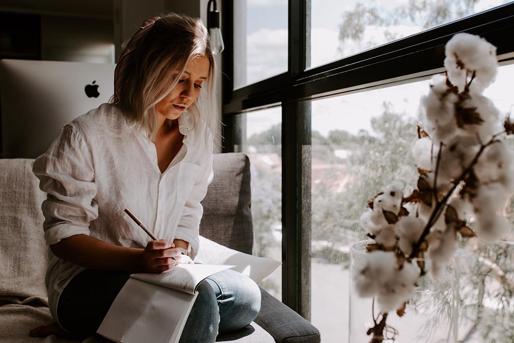 woman sat next to window, writing in a notepad